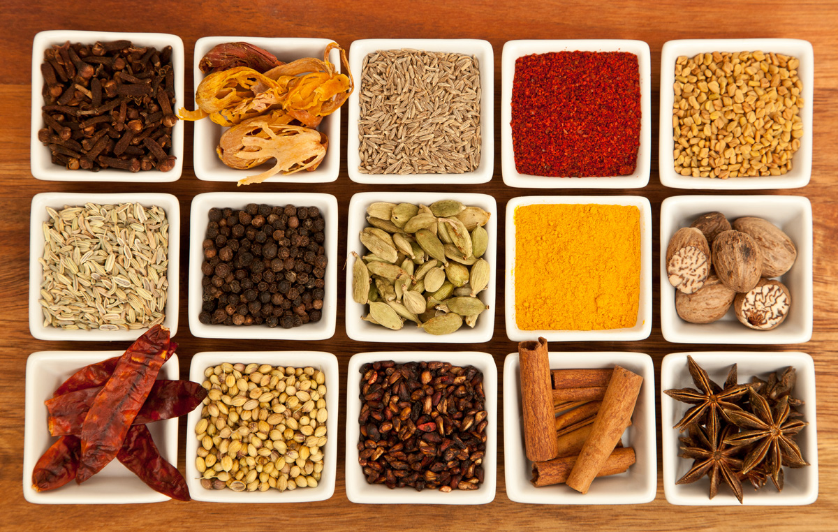 An overhead grid of colorful Indian spices in small bowls