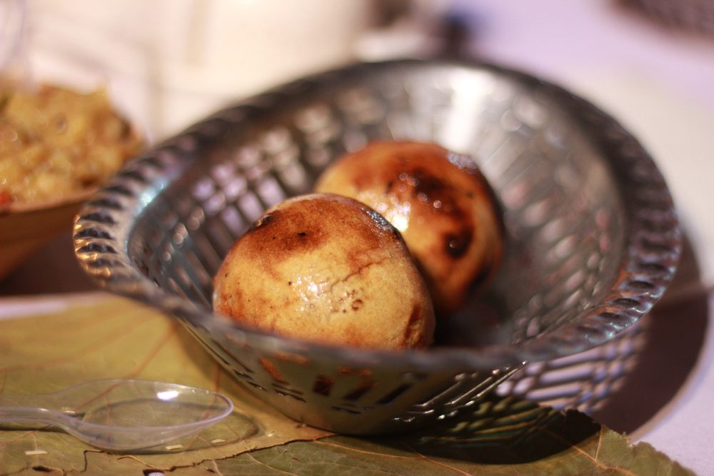 Two baked baatis glossy with ghee in a steel bowl, chokha behind