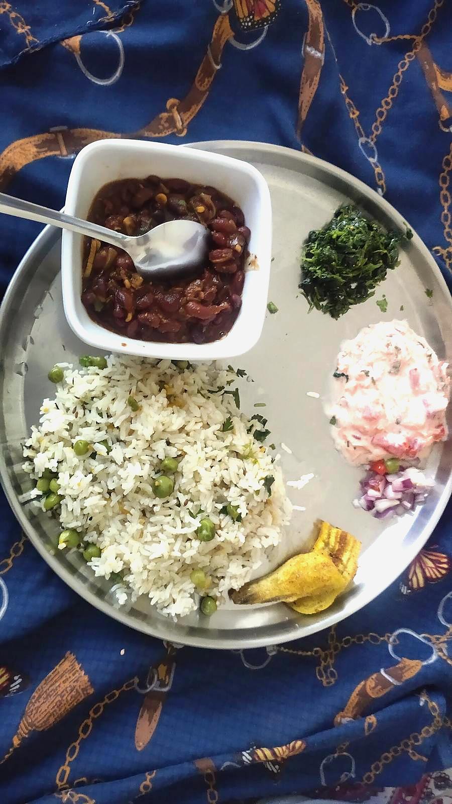 Rajma with jeera rice, saag and raita on a steel thali