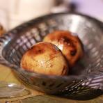Two baked baatis glossy with ghee in a steel bowl, chokha behind