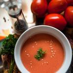 A bowl of tomato shorba topped with coriander and sesame, tomatoes behind